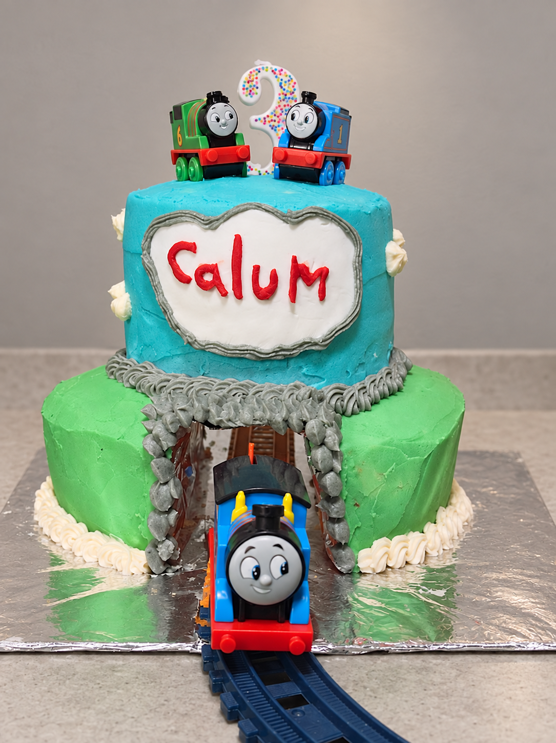 Blue and green Thomas the Train cake with a tunnel, railway track, and train toppers